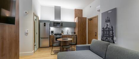 A modern kitchen with a dining area, a grey sofa, and a wall-mounted artwork.