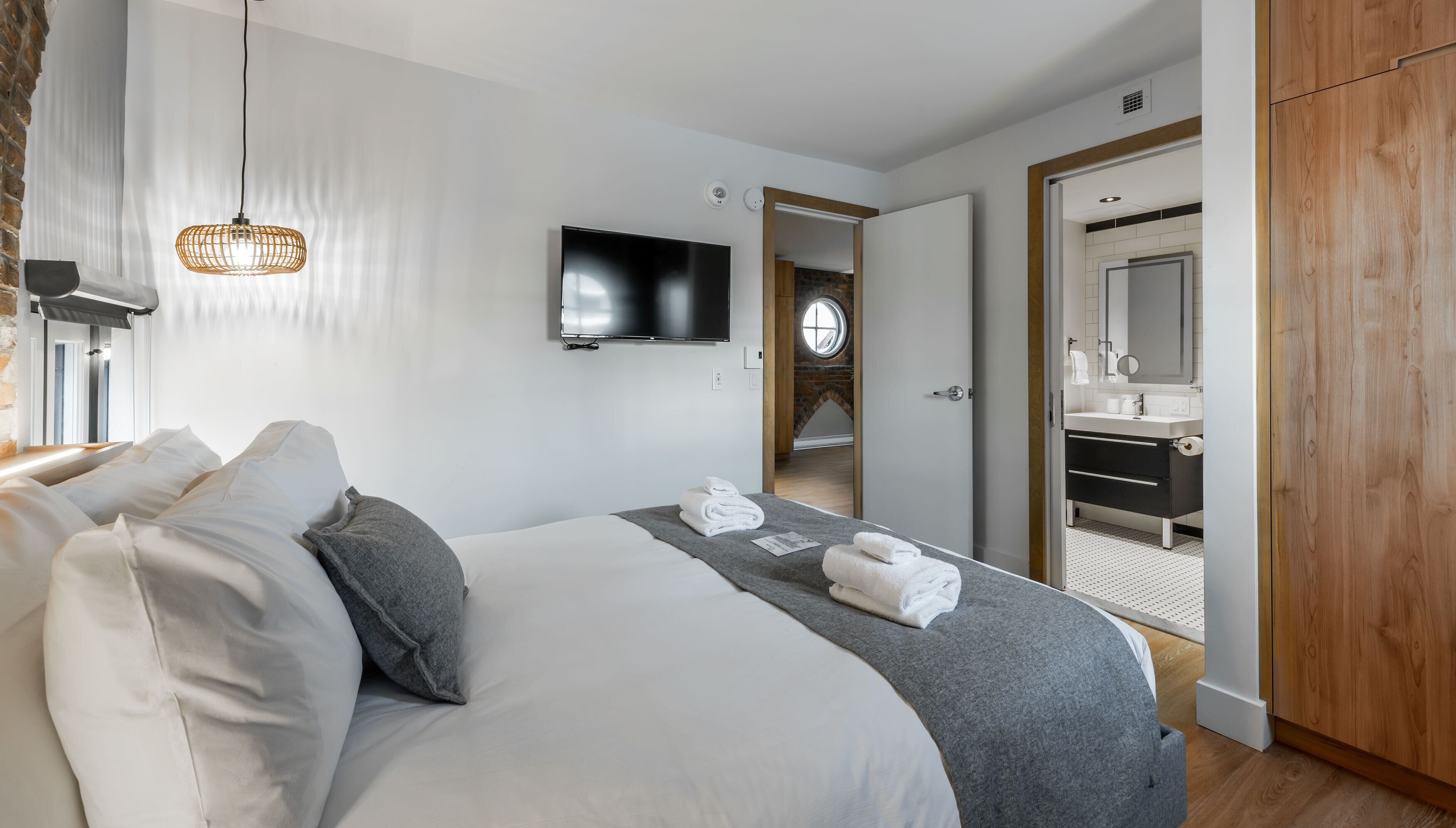 A modern hotel room with a large bed, a flat-screen TV, a wooden wardrobe, and a bathroom visible through an open door.