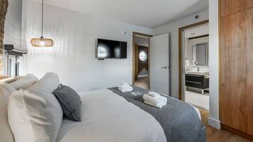 Una habitación de hotel moderna con una cama grande, un televisor de pantalla plana, un armario de madera y un baño visible a través de una puerta abierta.