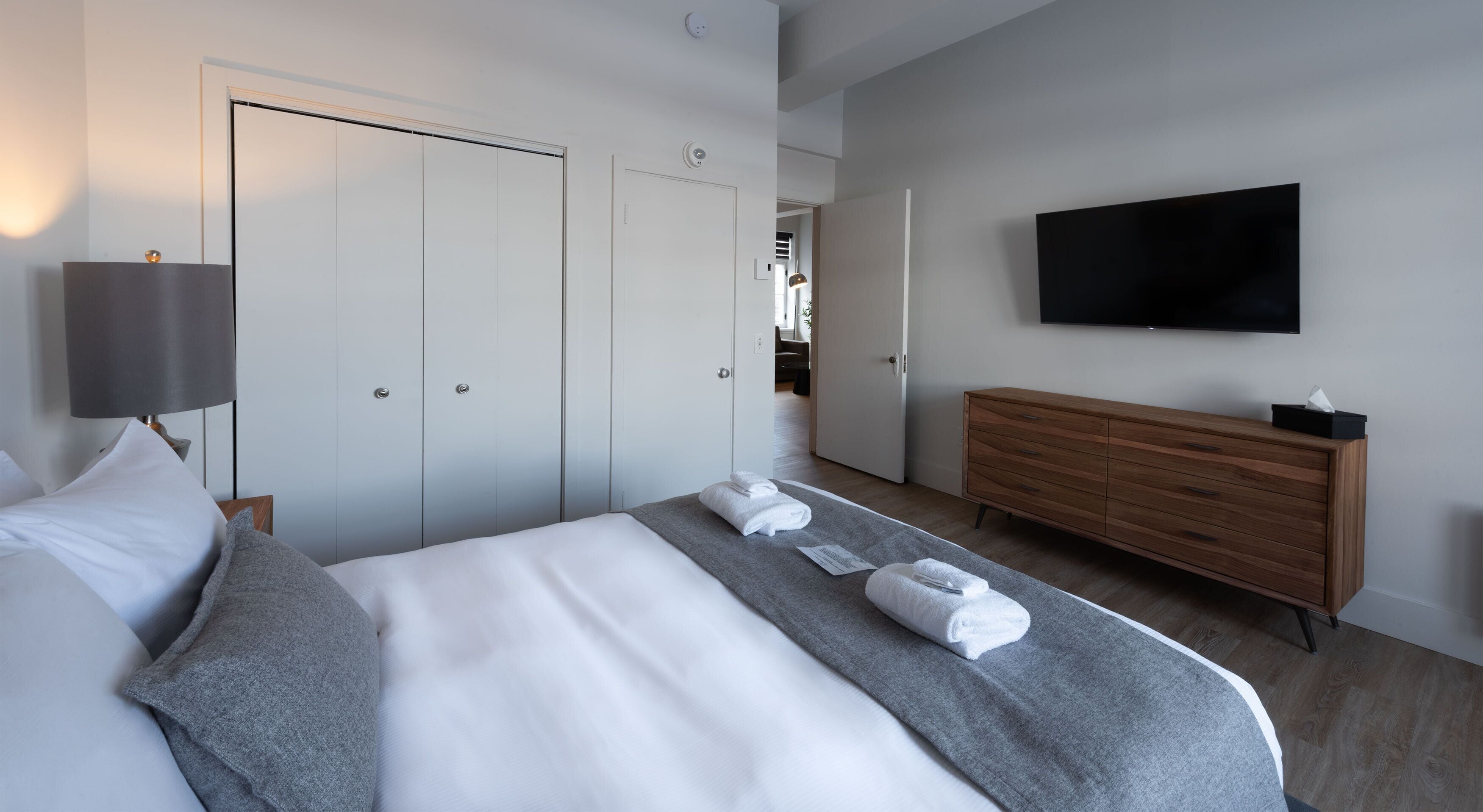 Quarto de hotel com cama, cômoda, televisão e armário.