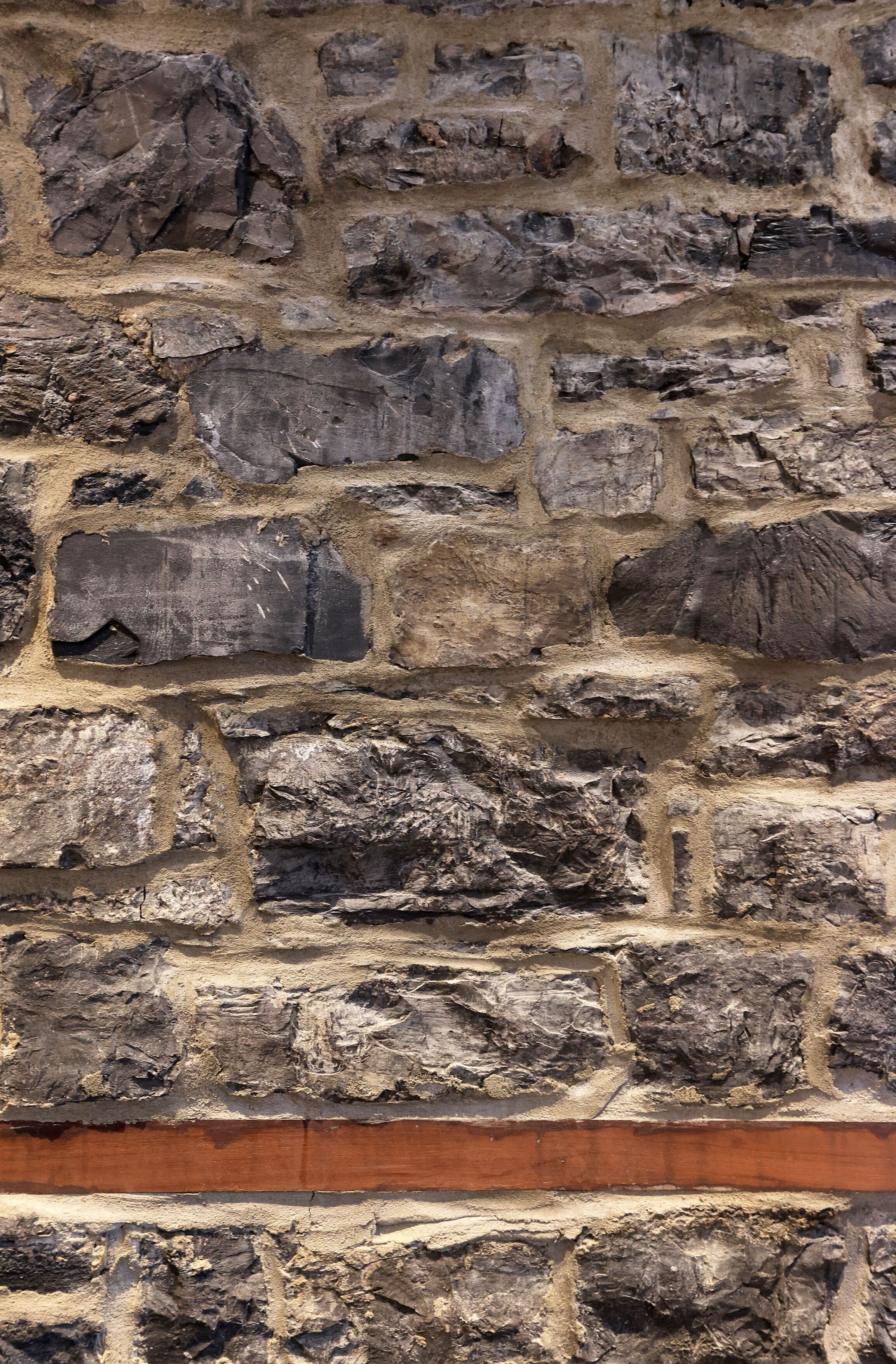 A close-up of a stone wall with irregularly shaped stones and a horizontal wooden beam.