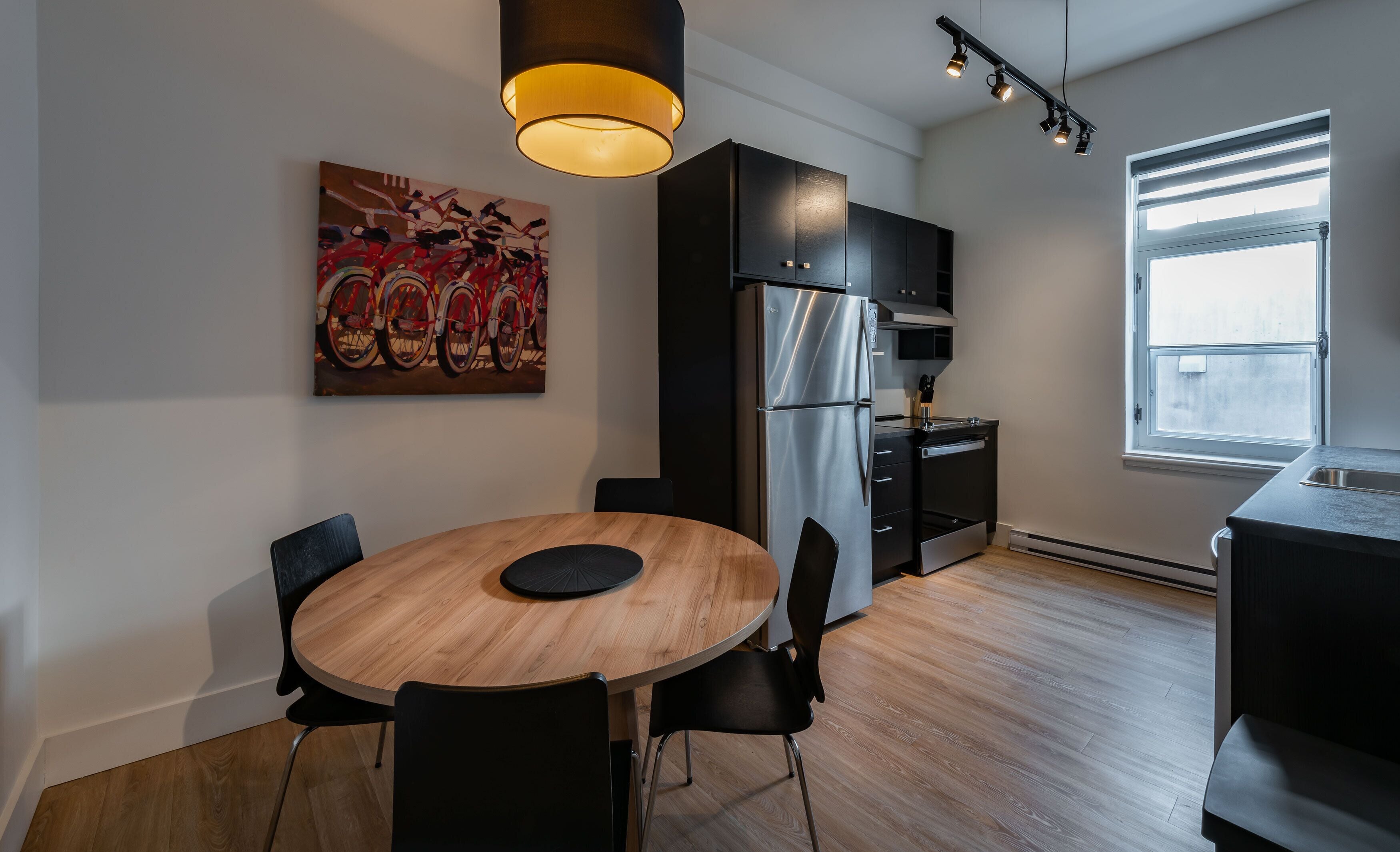 Een moderne keuken met een ronde houten tafel, zwarte stoelen, een roestvrijstalen koelkast en een groot raam.
