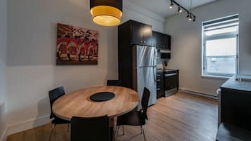 Een moderne keuken met een ronde houten tafel, zwarte stoelen, een roestvrijstalen koelkast en een groot raam.