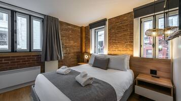 A modern hotel room with a large bed, a wooden headboard, a nightstand, and a window with a view of the city.