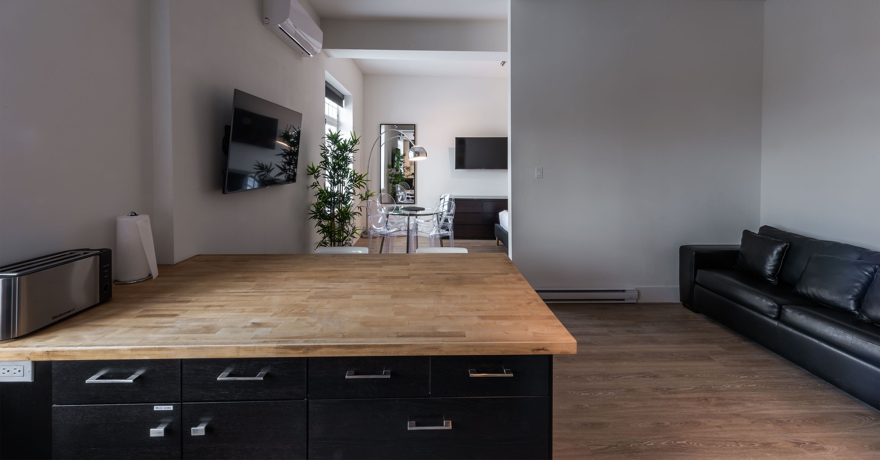A modern kitchen with a wooden countertop, black cabinets, and a dining area with a table and chairs.