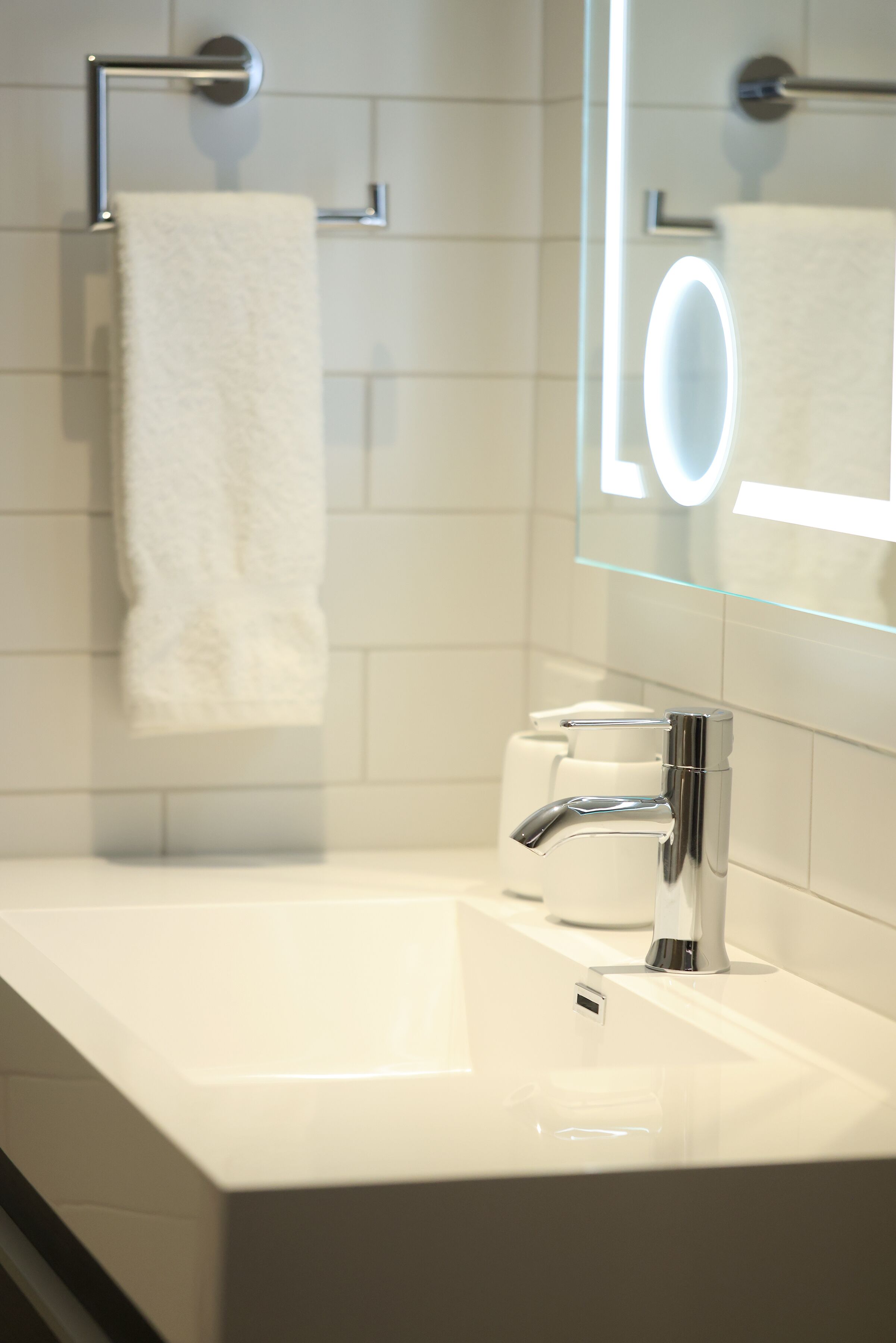 Un baño moderno con lavamanos blanco, grifo cromado y espejo de vidrio con luz.