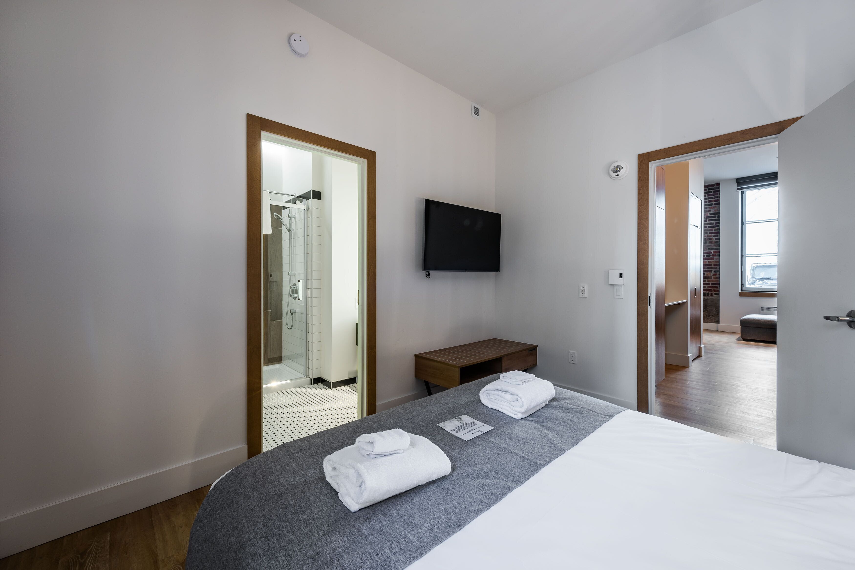 Habitación de hotel moderna con una cama grande, un televisor de pantalla plana, un banco de madera y vistas a la ciudad desde la ventana.