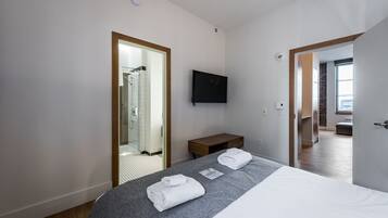 Habitación de hotel moderna con una cama grande, un televisor de pantalla plana, un banco de madera y vistas a la ciudad desde la ventana.