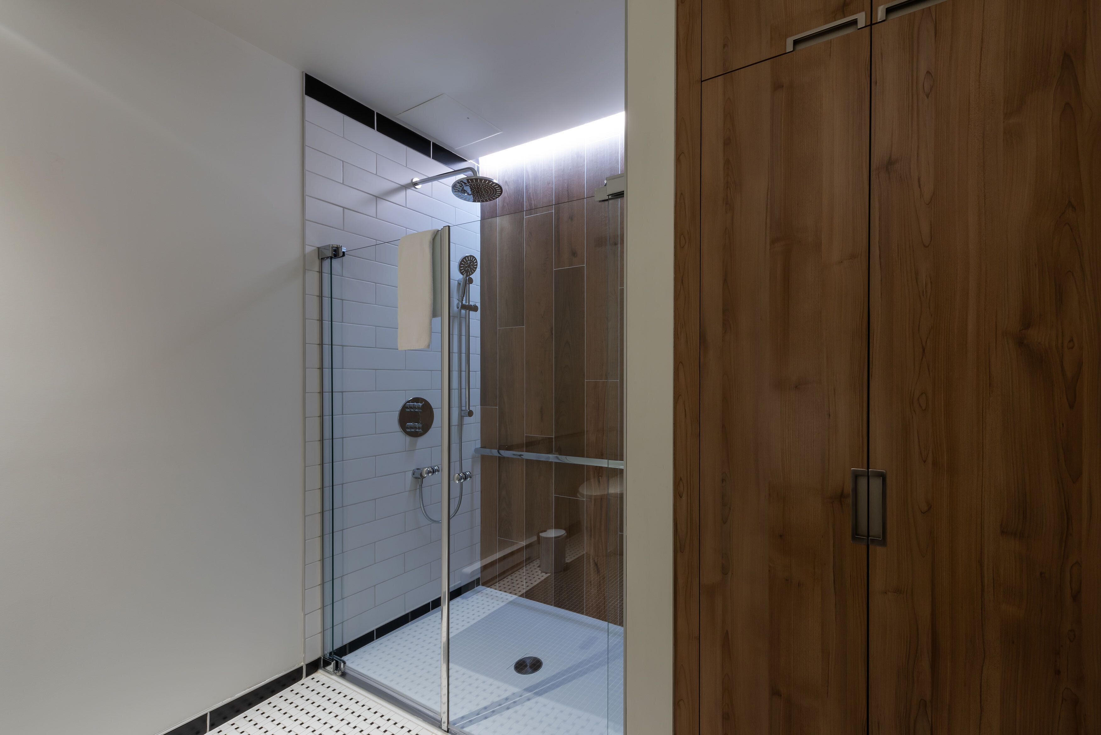 A modern bathroom with a glass-enclosed shower, white tiled walls, and a wooden wardrobe.