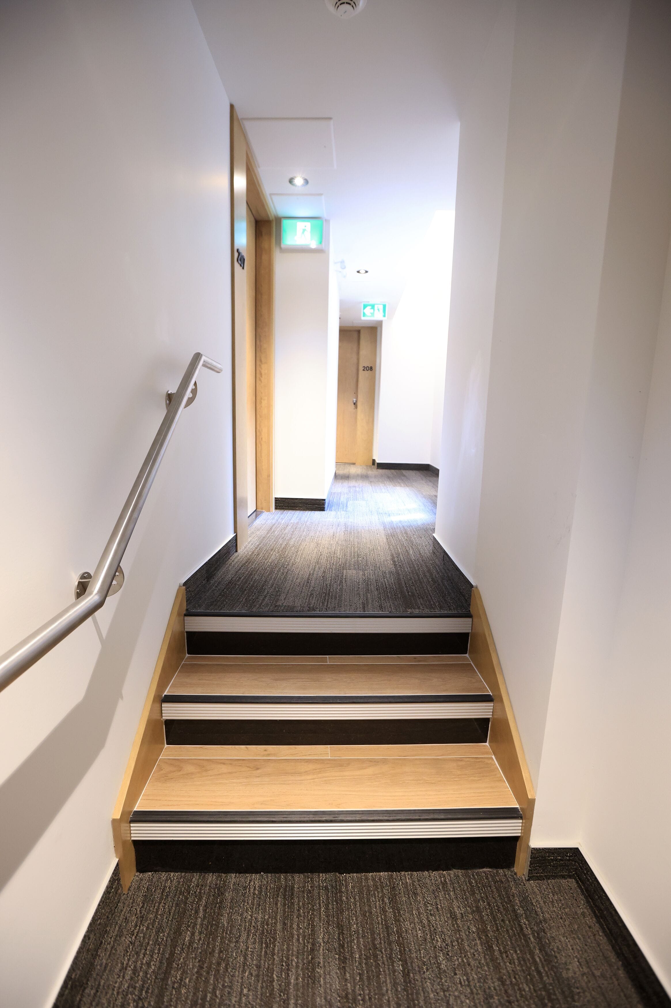 Una escalera estrecha alfombrada con barandilla que conduce a una puerta con el número 208.