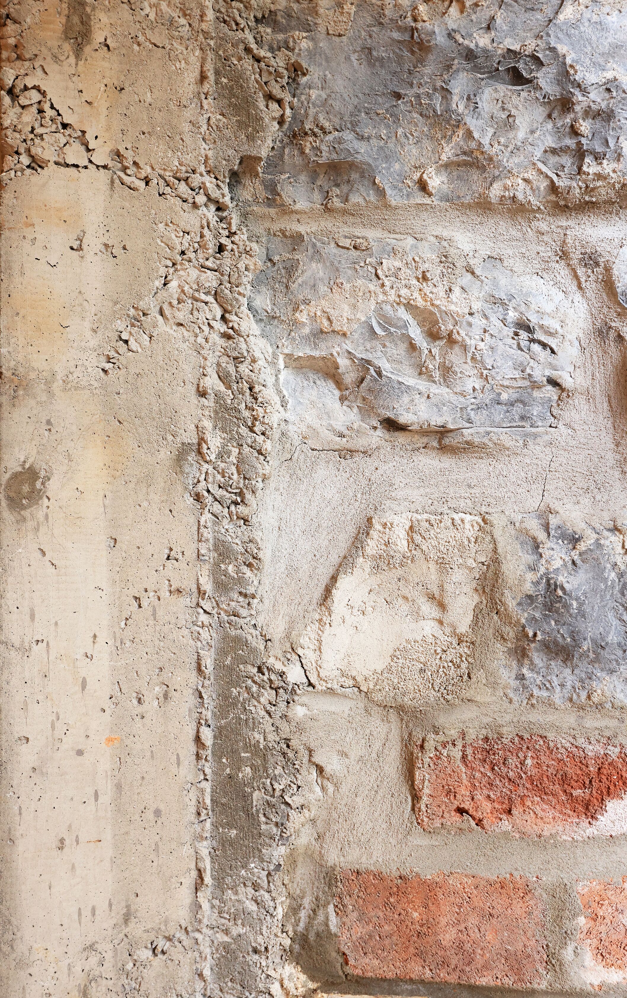 Primer plano de una pared con textura, mostrando grietas y capas de distintos materiales, como ladrillo y enlucido.