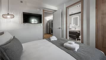 Quarto de hotel moderno com cama, televisão, banheiro com espelho e cozinha compacta.