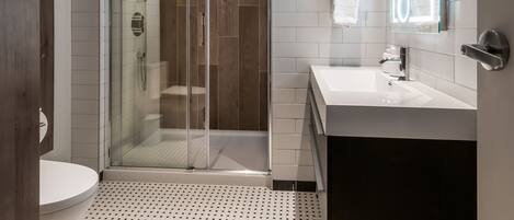 A modern bathroom with a glass-enclosed shower, a white sink, and a large mirror.