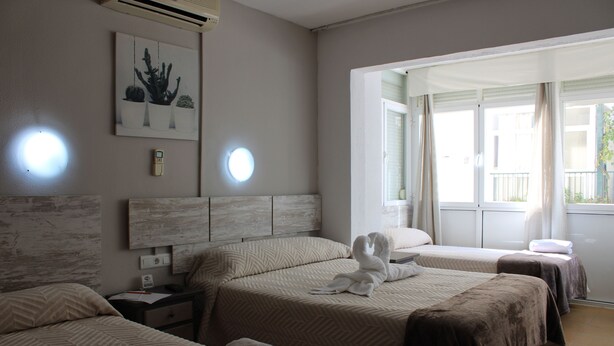 Ein Hotelzimmer mit drei Betten, einem großen Fenster und einem Wandbild.