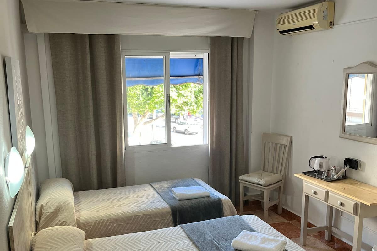 Quarto de hotel com duas camas, uma escrivaninha, uma cadeira e uma janela com vista para o exterior.