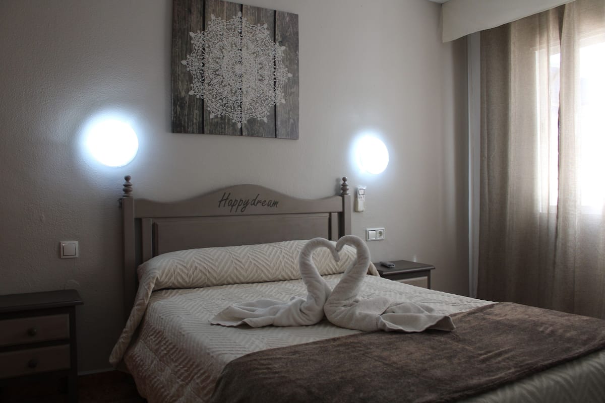 Quarto de hotel com cama, mesa de cabeceira, obra de arte na parede e janela com cortinas.
