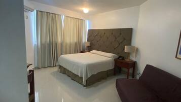 A hotel room with a bed, bedside tables, a sofa, a chair, and a window with curtains.