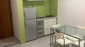 A compact kitchen with a refrigerator, stove, and white cabinets.