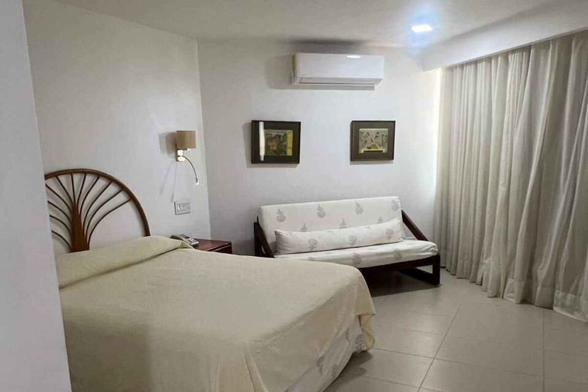 Een hotelkamer met een bed, een bank, een wandairconditioner en een lamp.