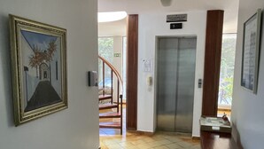 Hotellin aula, jossa on kiillotettu lattia, seinällä taulu, vastaanottotiski ja hissi.