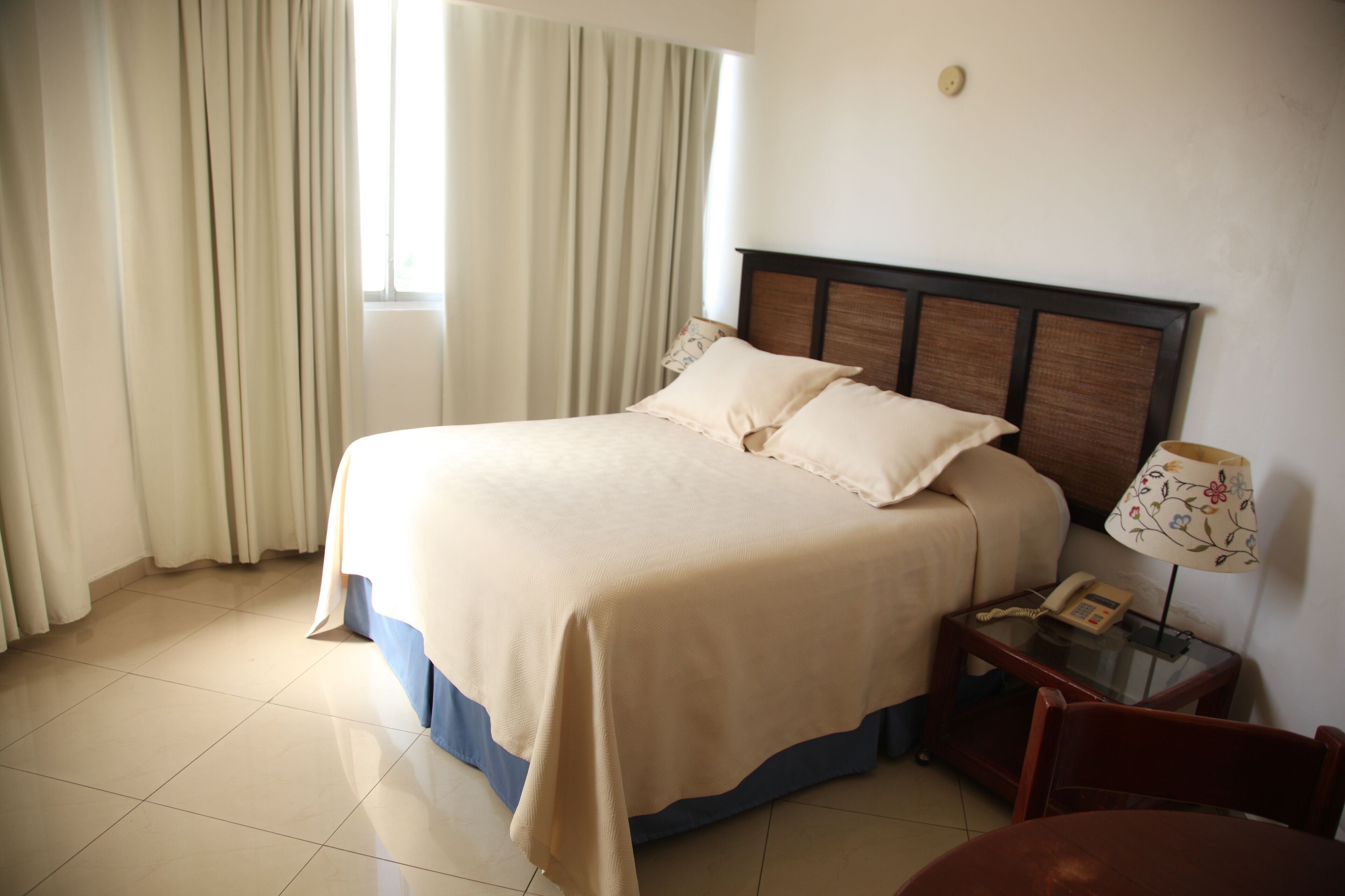A hotel room with a bed, a bedside table with a lamp, and a chair.