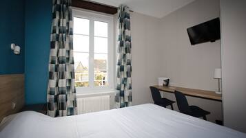 A hotel room with a bed, a desk, two chairs, a TV, and a window with curtains.
