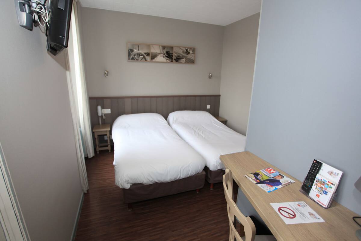 Een hotelkamer met twee bedden, een houten bureau, een flatscreen televisie en een kunstwerk aan de muur.