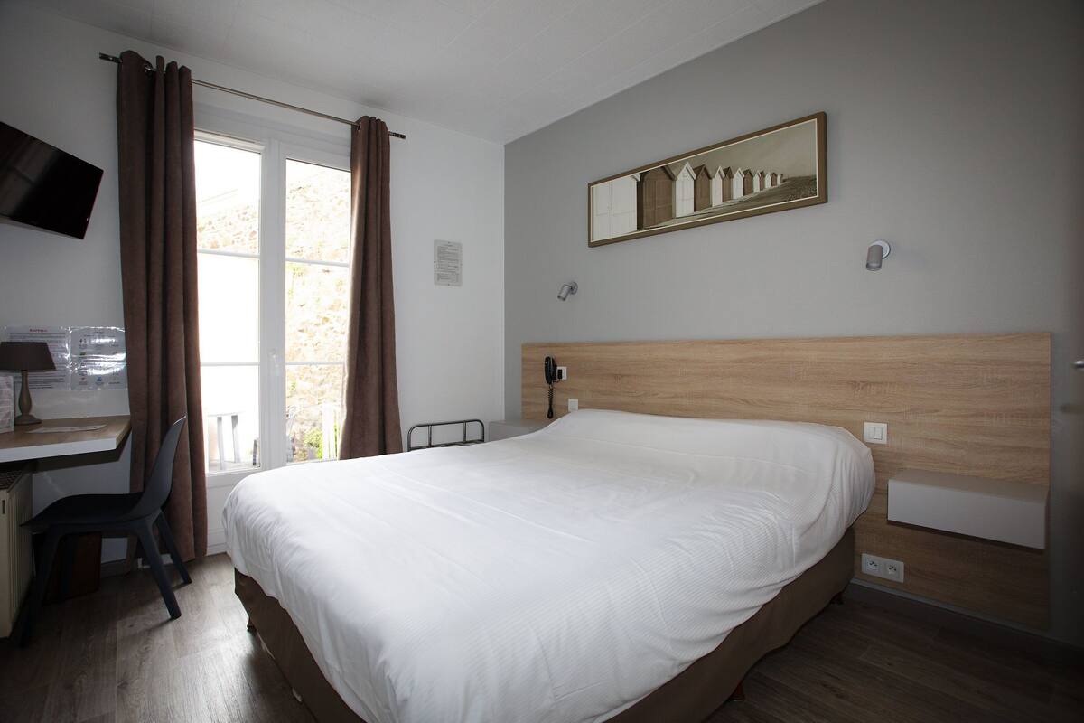Hotelkamer met een bed, een bureau, een stoel, een televisie, een raam met gordijnen en een spiegel aan de muur.