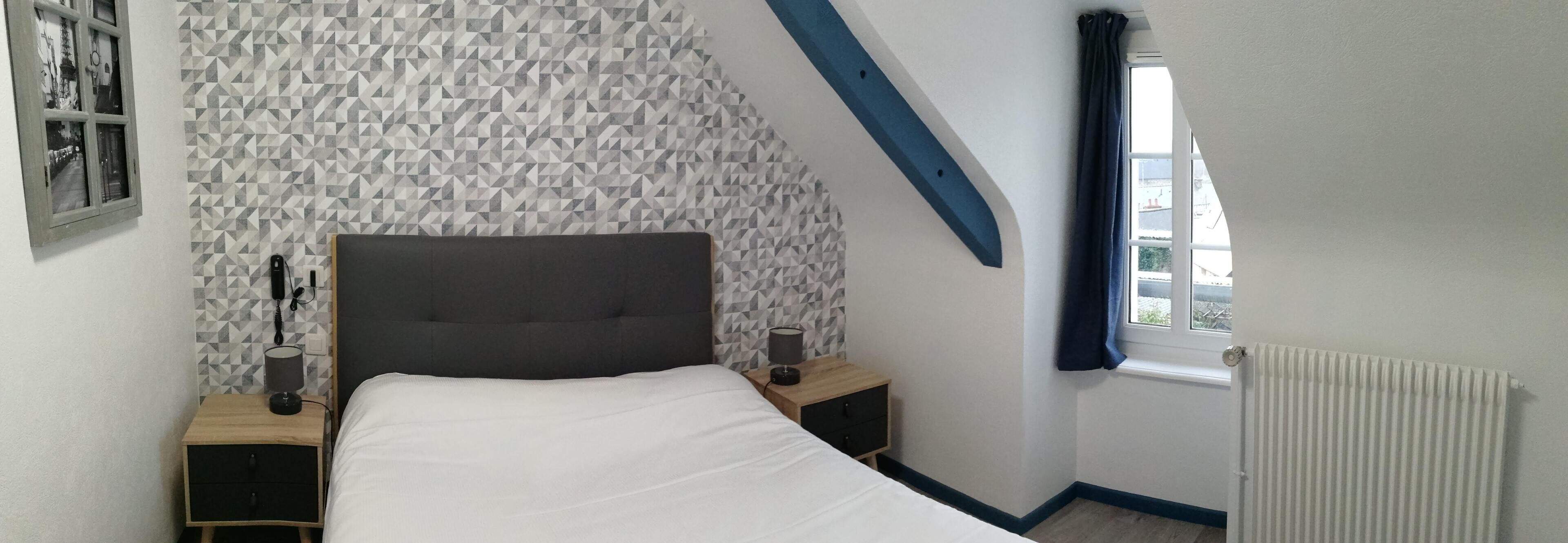 Un dormitorio con una cama, una mesita de noche, una lámpara, un marco de fotos, una ventana con cortinas y un radiador.