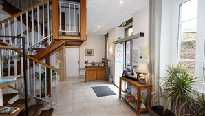 Un hall de hotel con escalera de madera, mostrador de recepción y plantas en macetas.