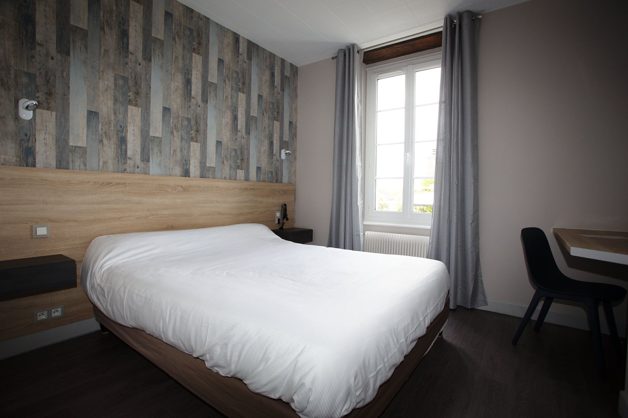 A neatly made bed in a hotel room with a wooden headboard, a desk, and a chair.