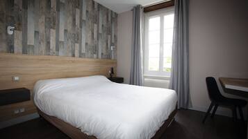 A neatly made bed in a hotel room with a wooden headboard, a desk, and a chair.