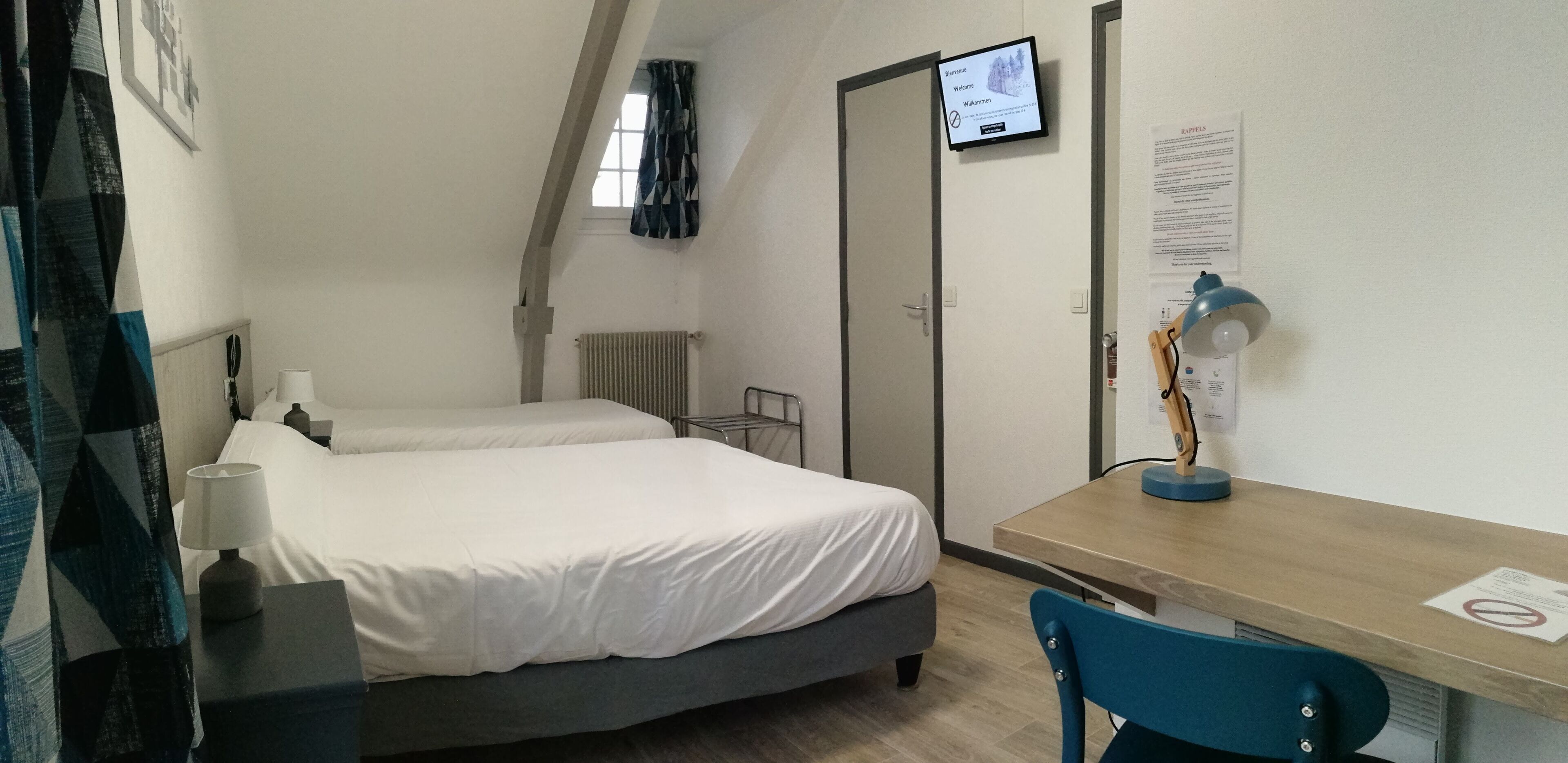 Habitación de hotel con cama, escritorio, silla, televisor y ventana con cortinas.