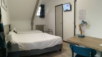 Habitación de hotel con cama, escritorio, silla, televisor y ventana con cortinas.