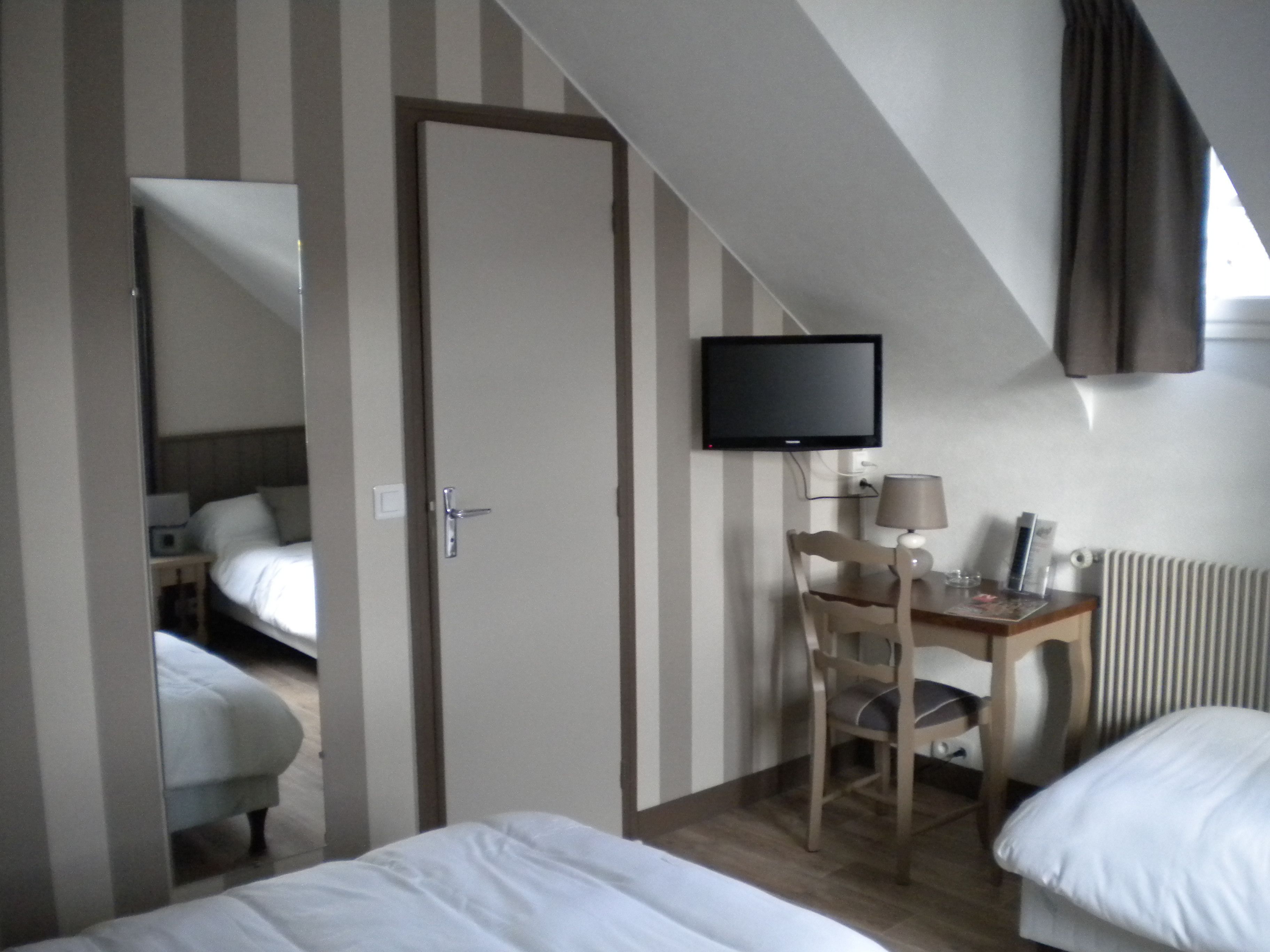 A hotel room with a bed, a desk with a chair, a television, and a window with curtains.