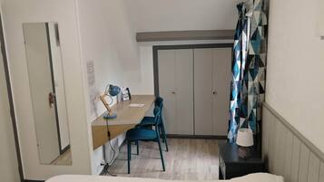 Una habitación pequeña y funcional con escritorio, dos sillas, lámpara y armario.