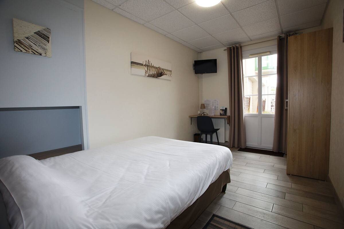Een hotelkamer met een bed, bureau, stoel, televisie en een deur.
