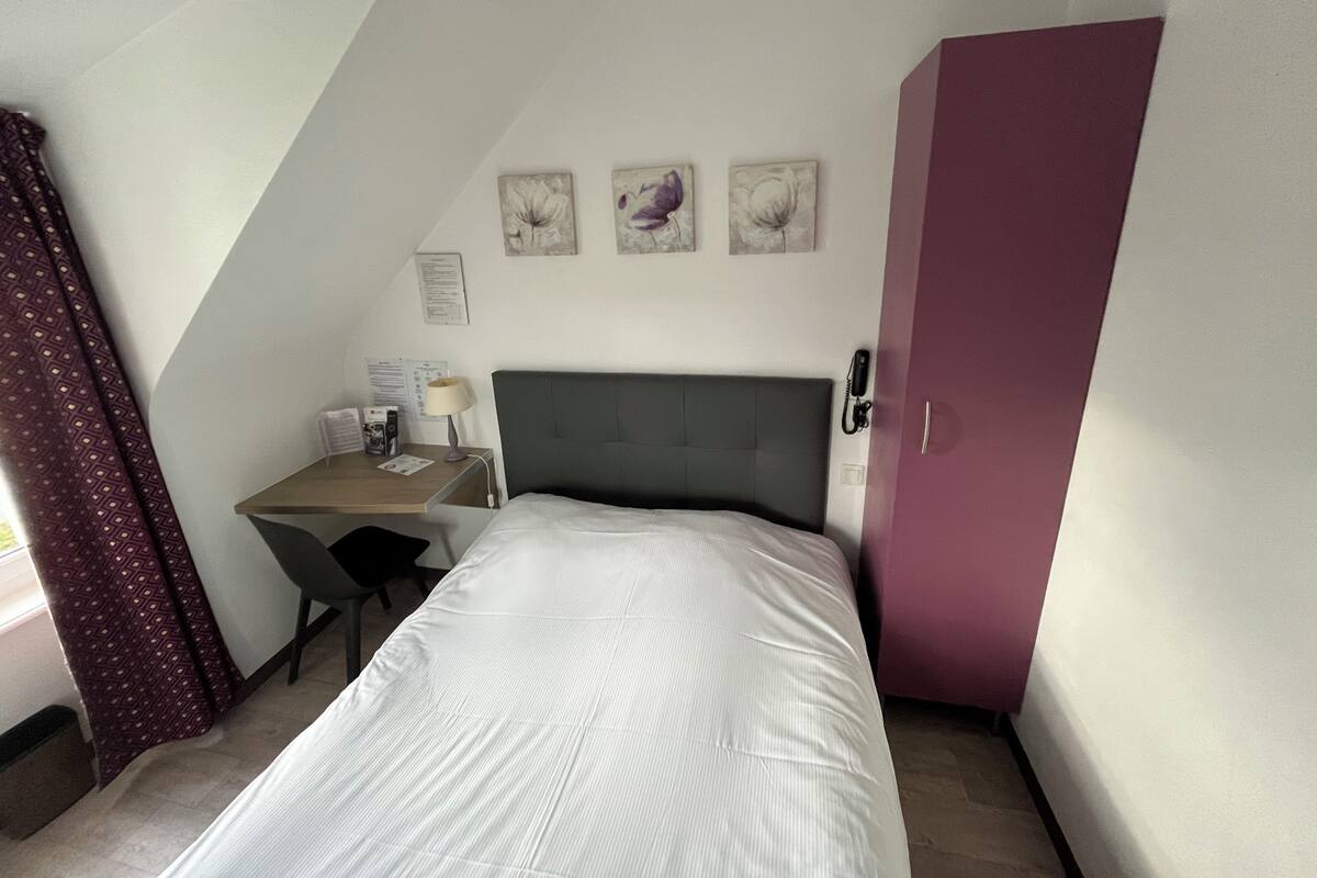 Een compacte, netjes ingerichte kamer met een bed, een bureau en een kledingkast.