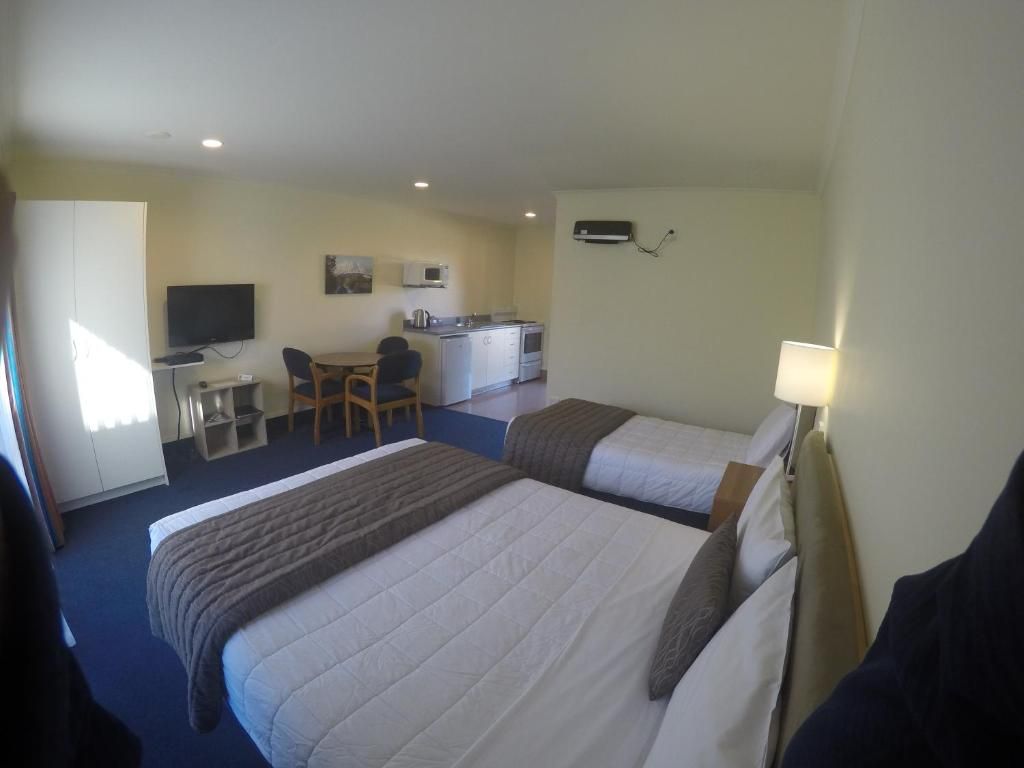 A hotel room with two beds, a desk, a chair, a television, and a kitchenette.