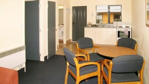 Una cocina compacta con estufa y fregadero, una zona de comedor con cuatro sillas, y una puerta que da a otra habitación.