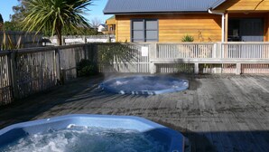 Una terraza de madera con dos tinas de hidromasaje y una casa al fondo.