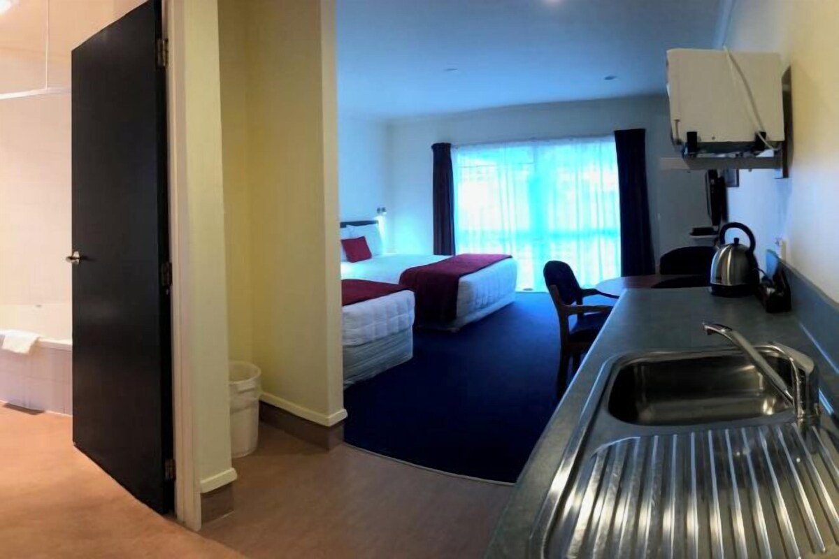 A hotel room with a bed, a desk with a sink, a chair, and a window with curtains.