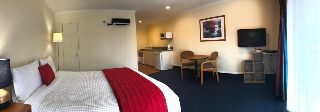 Una habitación de hotel con una cama, un escritorio, una silla, un televisor y una kitchenette.