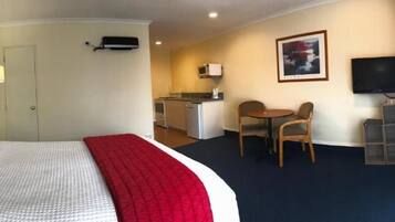 Una habitación de hotel con una cama, un escritorio, una silla, un televisor y una kitchenette.