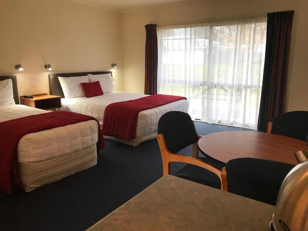 Quarto de hotel com duas camas, uma mesa de jantar e vista para o exterior.