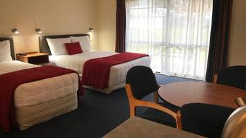 Quarto de hotel com duas camas, uma mesa de jantar e vista para o exterior.