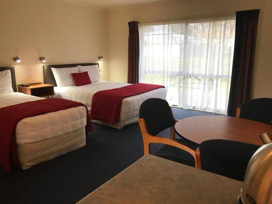 Quarto de hotel com duas camas, uma mesa de jantar e vista para o exterior.