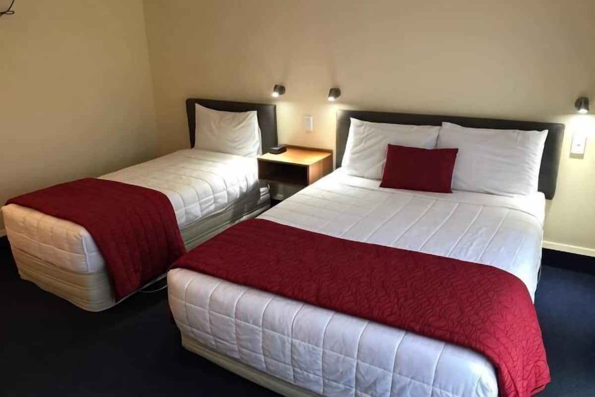 Quarto de hotel com duas camas, cada uma com um cobertor vermelho, uma mesa de cabeceira e luminárias fixadas na parede.