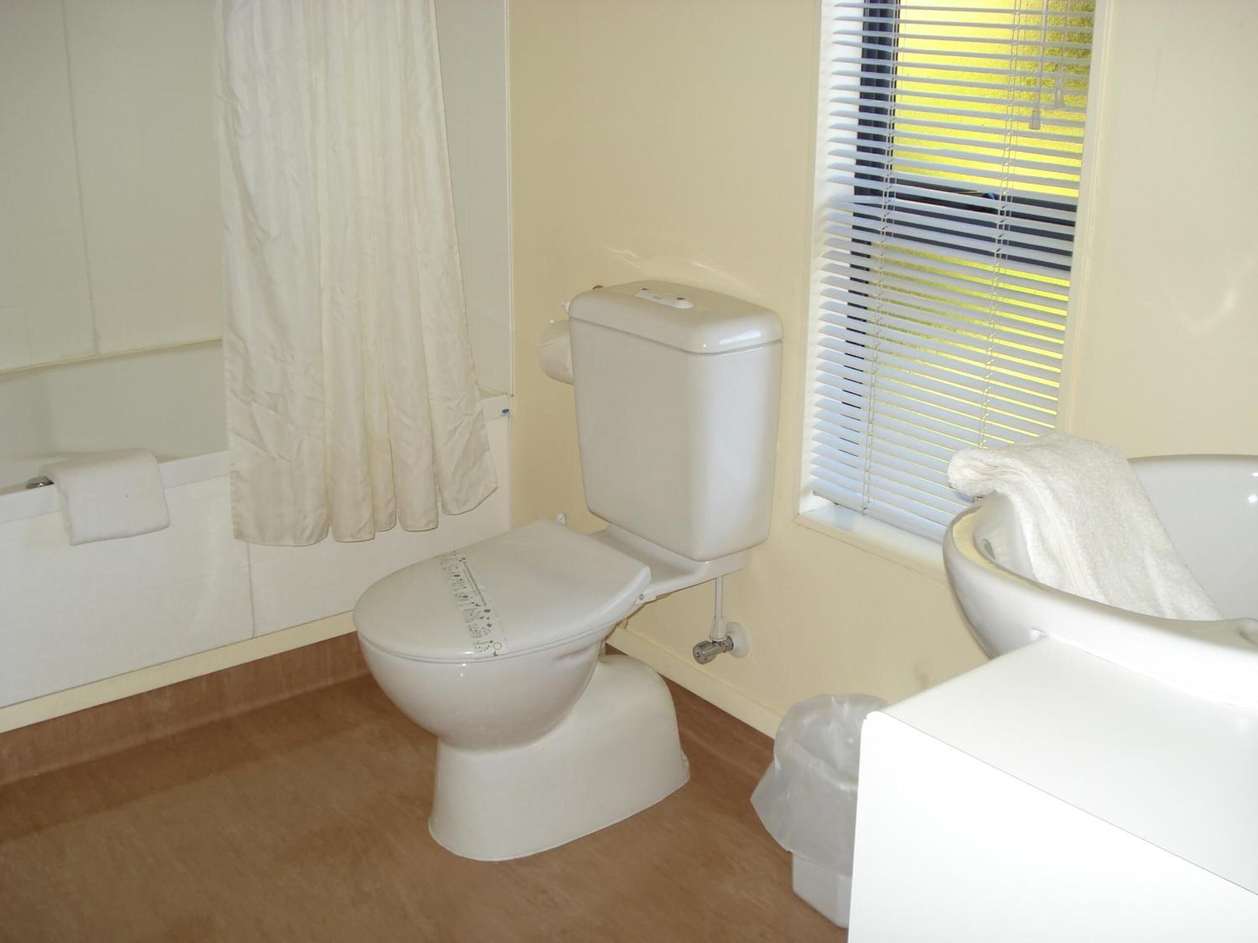 A bathroom with a toilet, a bathtub, and a window with blinds.