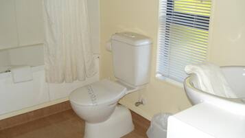 Ein Badezimmer mit Toilette, einer Badewanne und einem Fenster mit Jalousien.